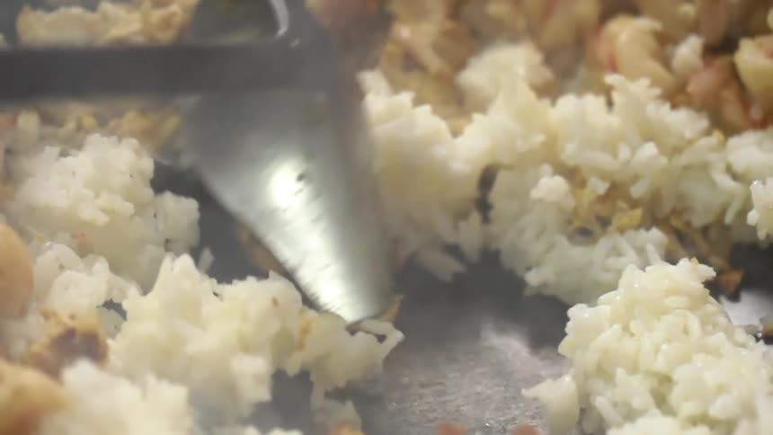 A chef stirs white rice and shrimps in a wok