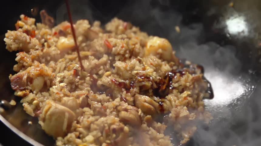 Soy sauce being poured on fried rice with chicken as it cooks