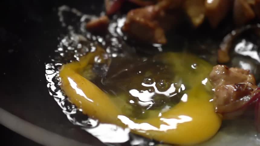 A raw egg drops into a pan with meat in it