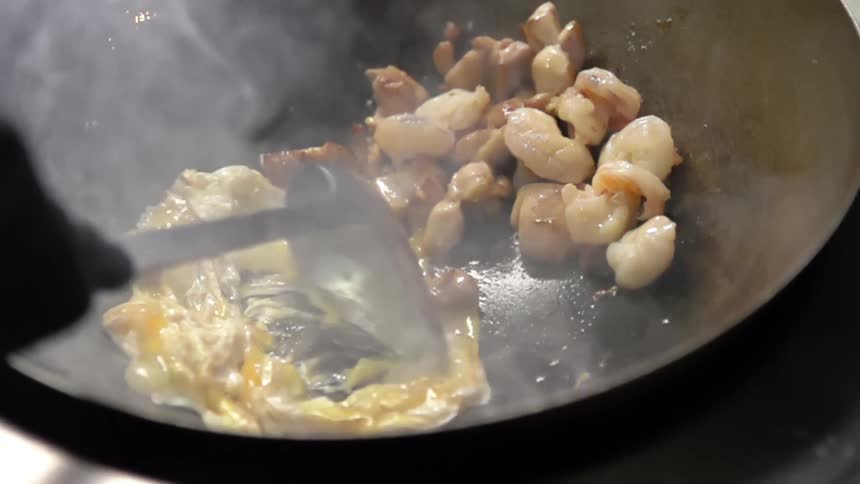 Eggs and shrimp being cooked in a wok with smoke