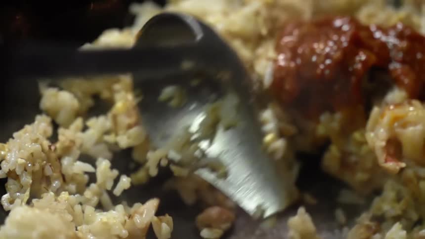 A pot spoon tossing rice and sauce in a pan with smoke coming off of it