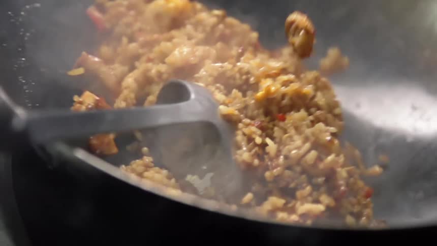 A person tossing fried rice in a wok with a metal ladle