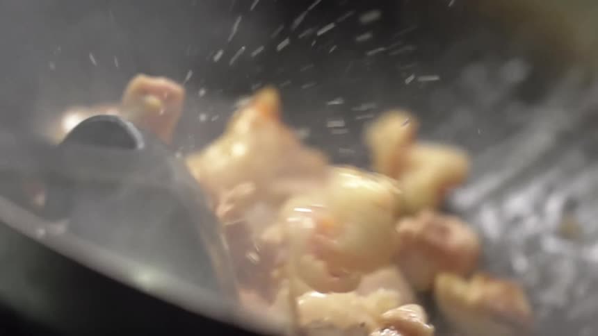 A person uses a metal ladle to toss the meat frying in a oily wok