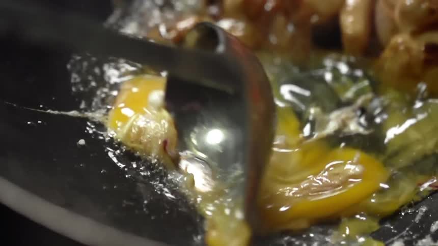 Metal spoon scrambles raw eggs in skillet