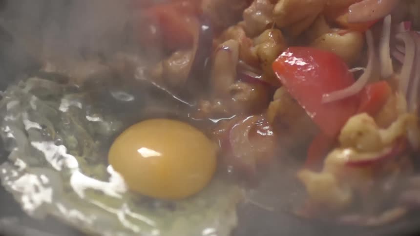 An egg is dropped into a wok with cooked vegetables