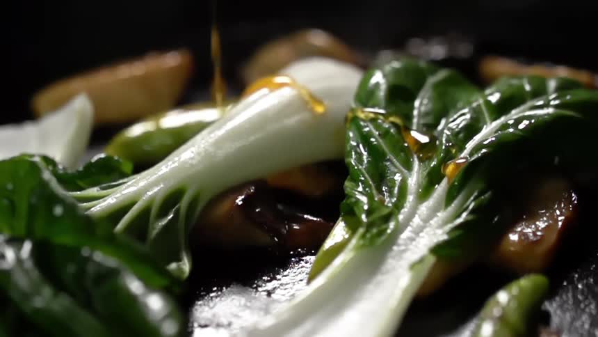 Oil pouring over mushrooms and bok choy being cooked over a hot grill
