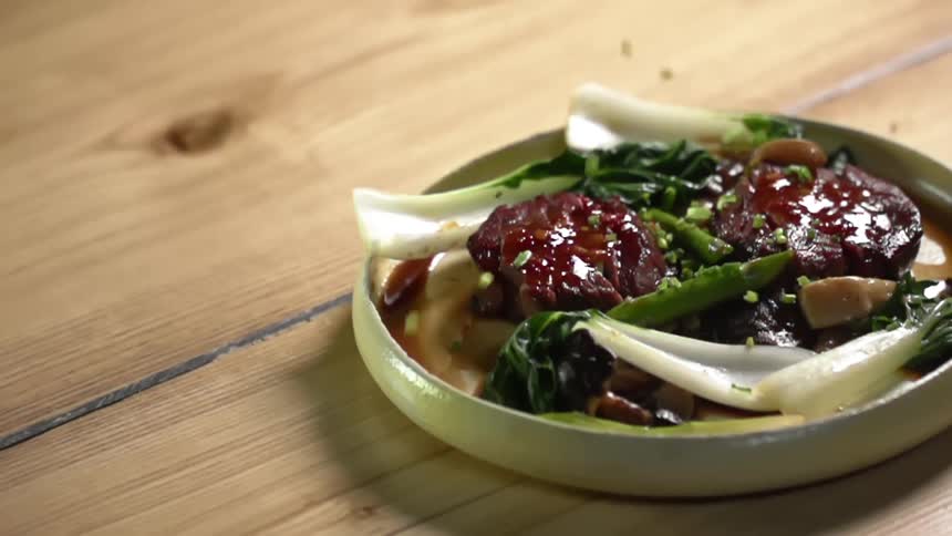 Seasoning and herbs are sprinkled over the top of steak and some steamed bok choy