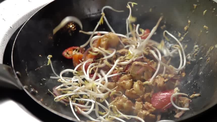 Bean sprouts falling into a pan of stir fried vegetables