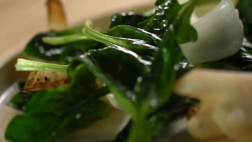 Spinach leaves fall onto a plate of cauliflower and bok choy