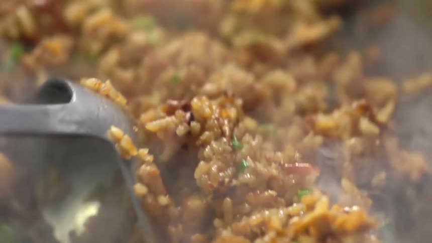 A rice meal cooking on a hot steaming wok stirred using a soup ladle