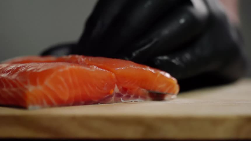 A person with gloves cutting salmon on a cutting board with a knife