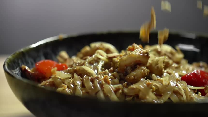 A bowl with noodles with crushed peanut falling onto it