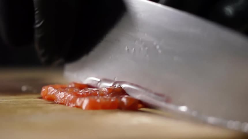 A person with black gloves cutting salmon with a knife on a cutting board