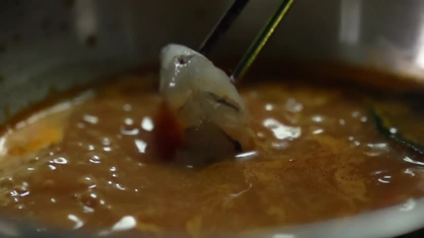 Chopsticks pick up a shrimp in broth and then drop it back in