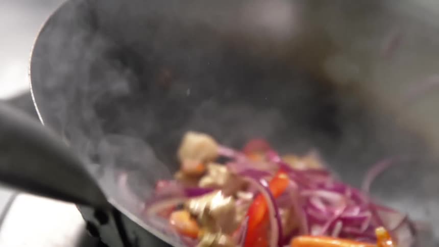 Steaming hot meat and vegetables are tossed in a work as they are being stir fried
