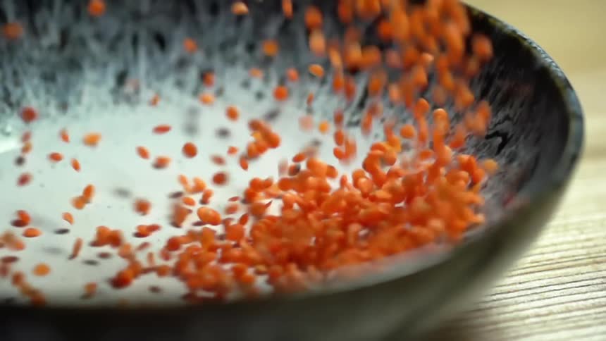 Red lentil pouring on a black and white ceramic bowl over a wooden table