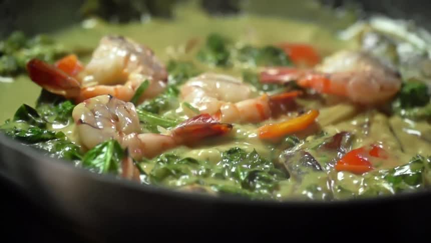 Metal skillet being jiggled to stir shrimp in curry