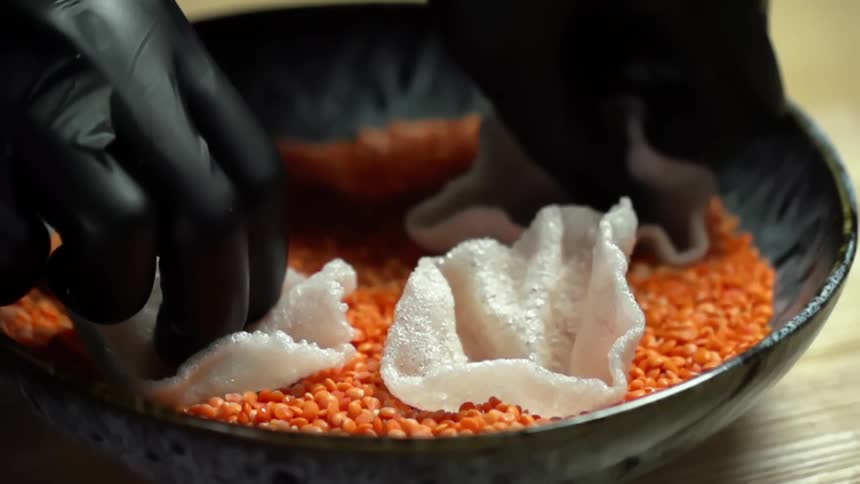 A person sets rice chips in a bowl of lentils