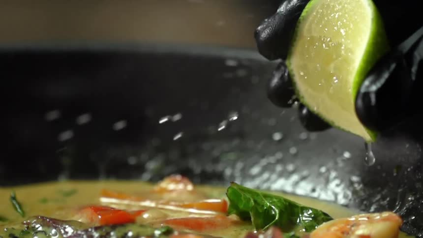 Person wearing black gloves squeezes lime juice onto curry in skillet