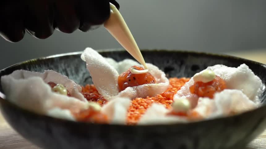 A person with black gloves adding cream to salmon in a rice chip