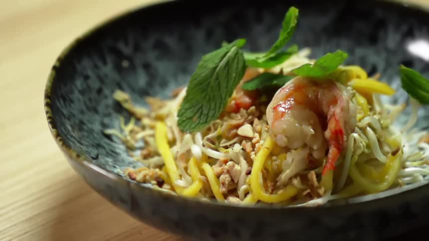 Mint leaves falling on a bowl with shrimps and sprouts