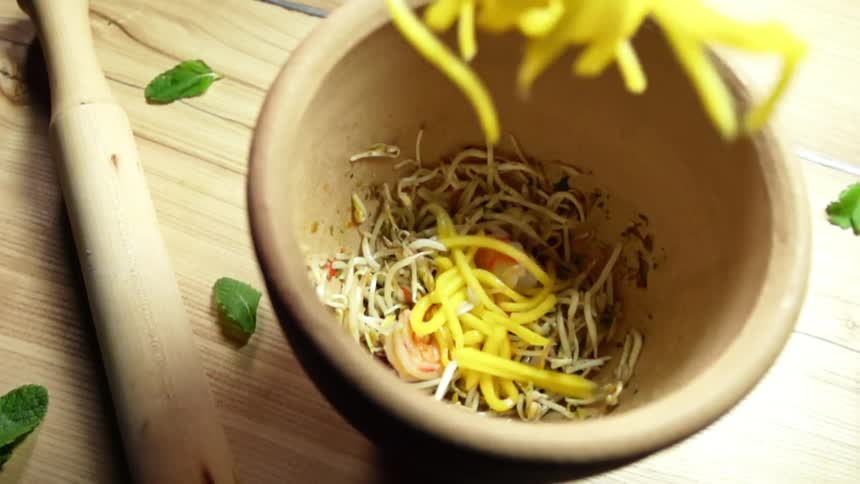 Noodles falling into a bowl with bean sprouts and shrimps