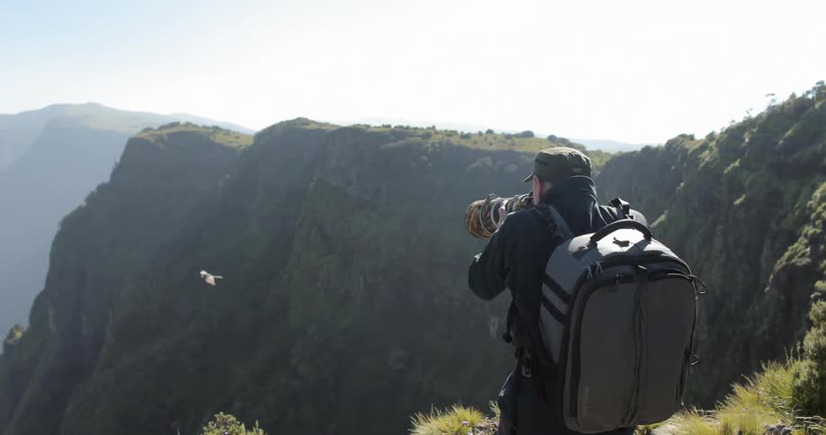 A man is photographing a bird flying near a mountain top