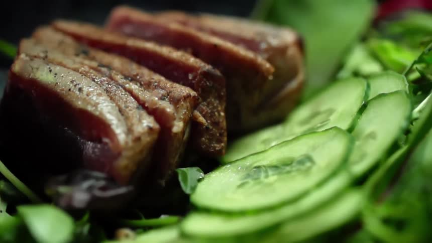 Placing a piece of sliced beef steak over a green salad