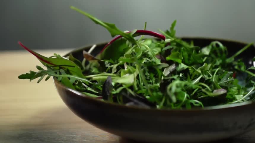 Leafy greens falling in slow motion into a ceramic bowl