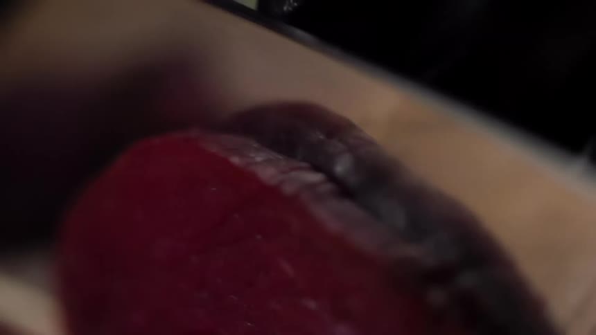 A person wearing a black glove slices tuna steak with a knife
