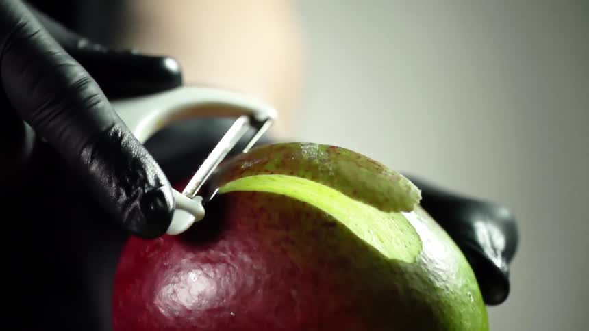 A person with black gloves peeling a mango with a peeler
