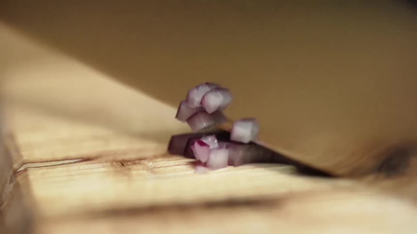 Sharp kitchen knife finely chopping onion on a wooden cutting board
