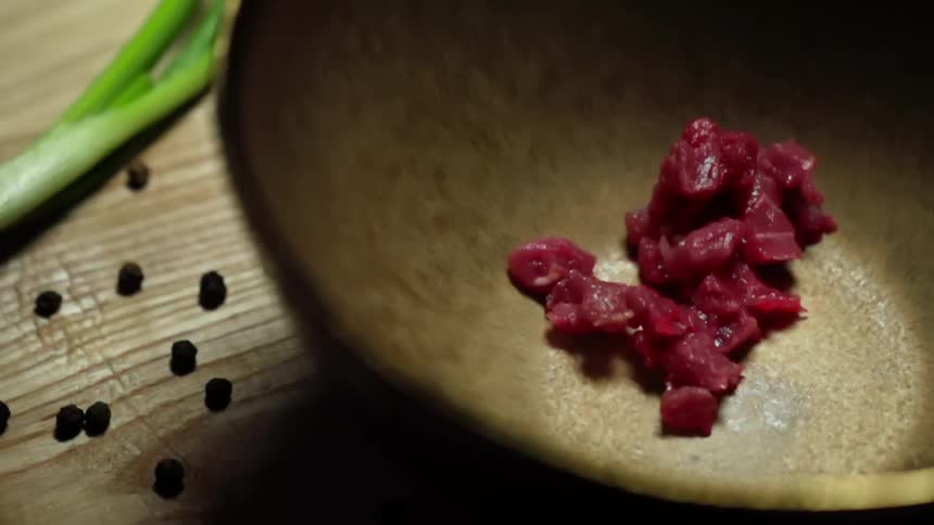 Chopped tuna falling inside a brown bowl over a wooden table