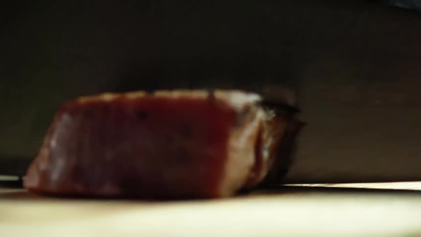 Cook with black gloves cuts tuna steak with a knife