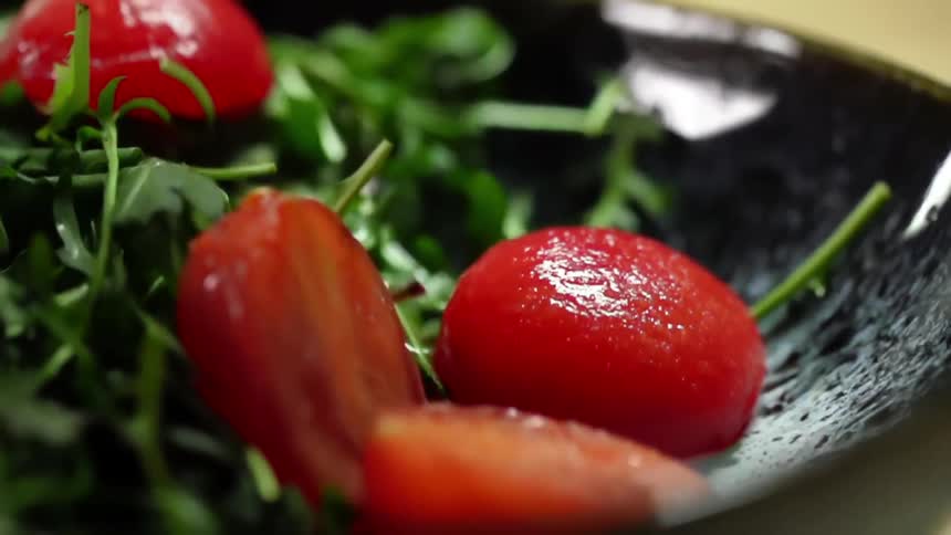 Sliced cherry tomatoes fall into a dish of vegetables
