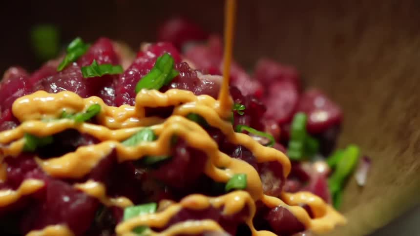 Yellow sauce drizzles across raw tuna mince in wooden bowl