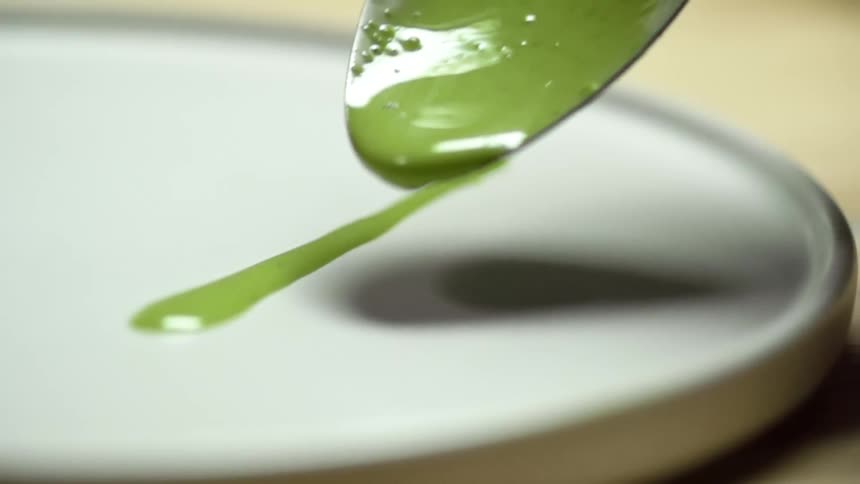 Small spoon serving thin lines of green sauce over a small white ceramic plate