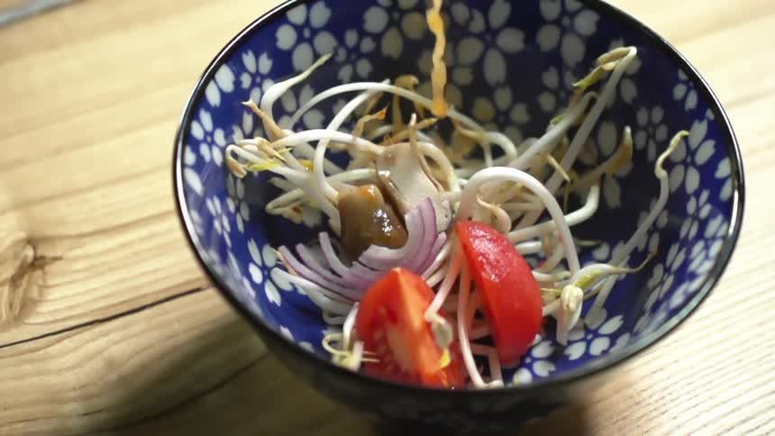 Yellow broth pours over bean sprouts and vegetables inside a blue ceramic bowl