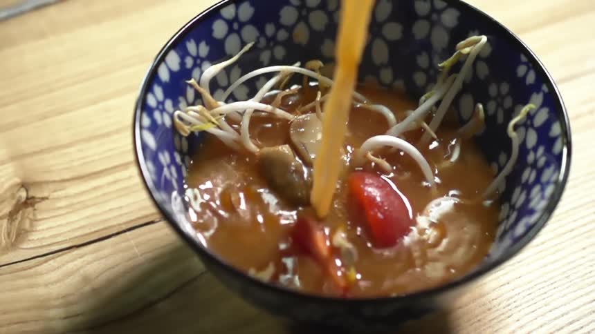 Broth being poured into a blue bowl containing bean sprouts and tomatoes