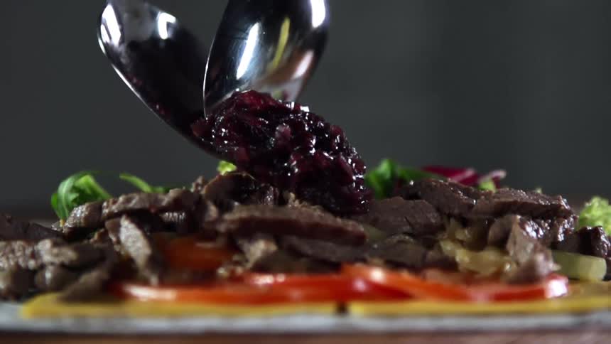 Serving jam with spoons over steak strips in a dish