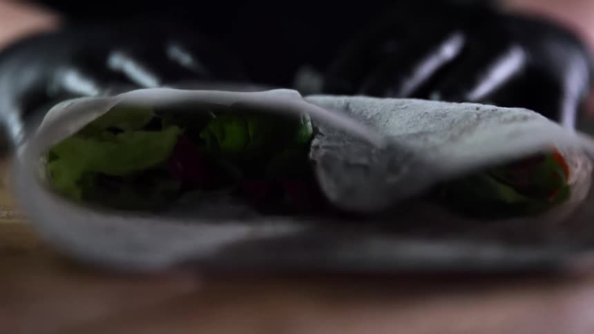 Person wearing black gloves folds leafy vegetables in wrapper