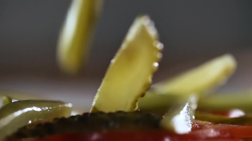 Close up of sliced pickles being dropped onto the meal