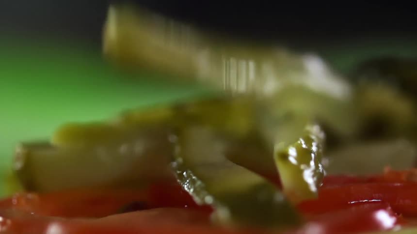 A slice of pickle falls onto a pile of garnish