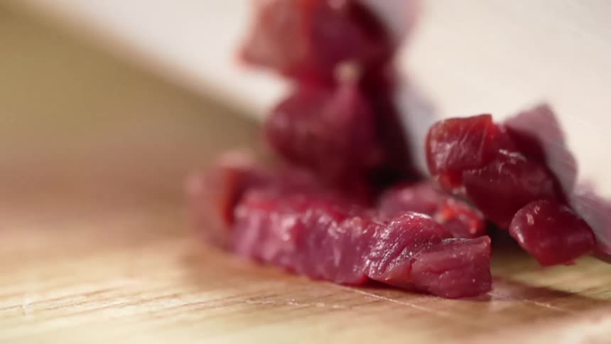 A knife slices and dices raw tuna on a wood cutting board