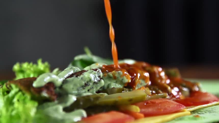 Pouring a red condiment onto a pile of food on a table