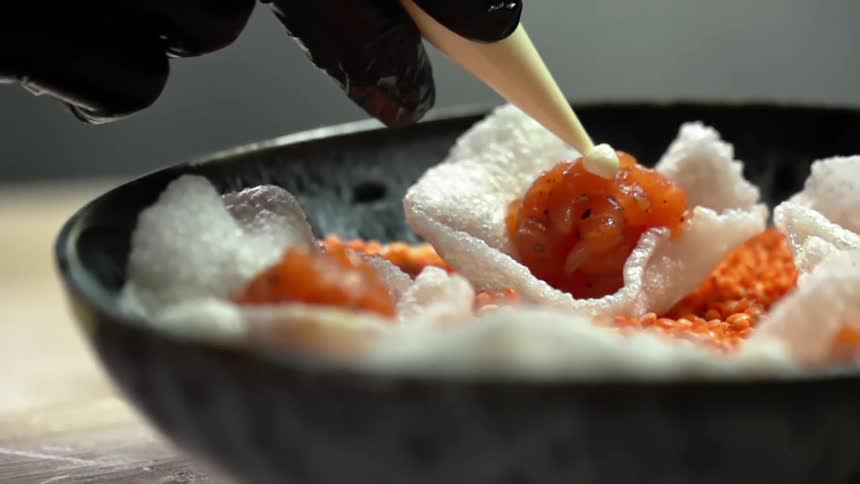A person with black gloves adding cream onto salmon in a rice chip