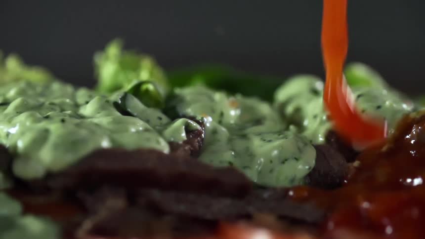 Red sauce splashing over sliced meat covered in guacamole