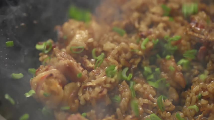 Chopped scallions fall over cooked rice with chicken on a steaming hot wok