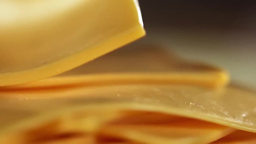 A gloved hand peels a slice of cheddar cheese from a pile of a cheese