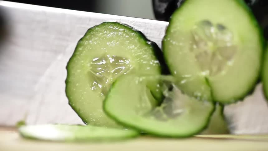 A cook cuts a cucumber with a sharp knife on a cutting board
